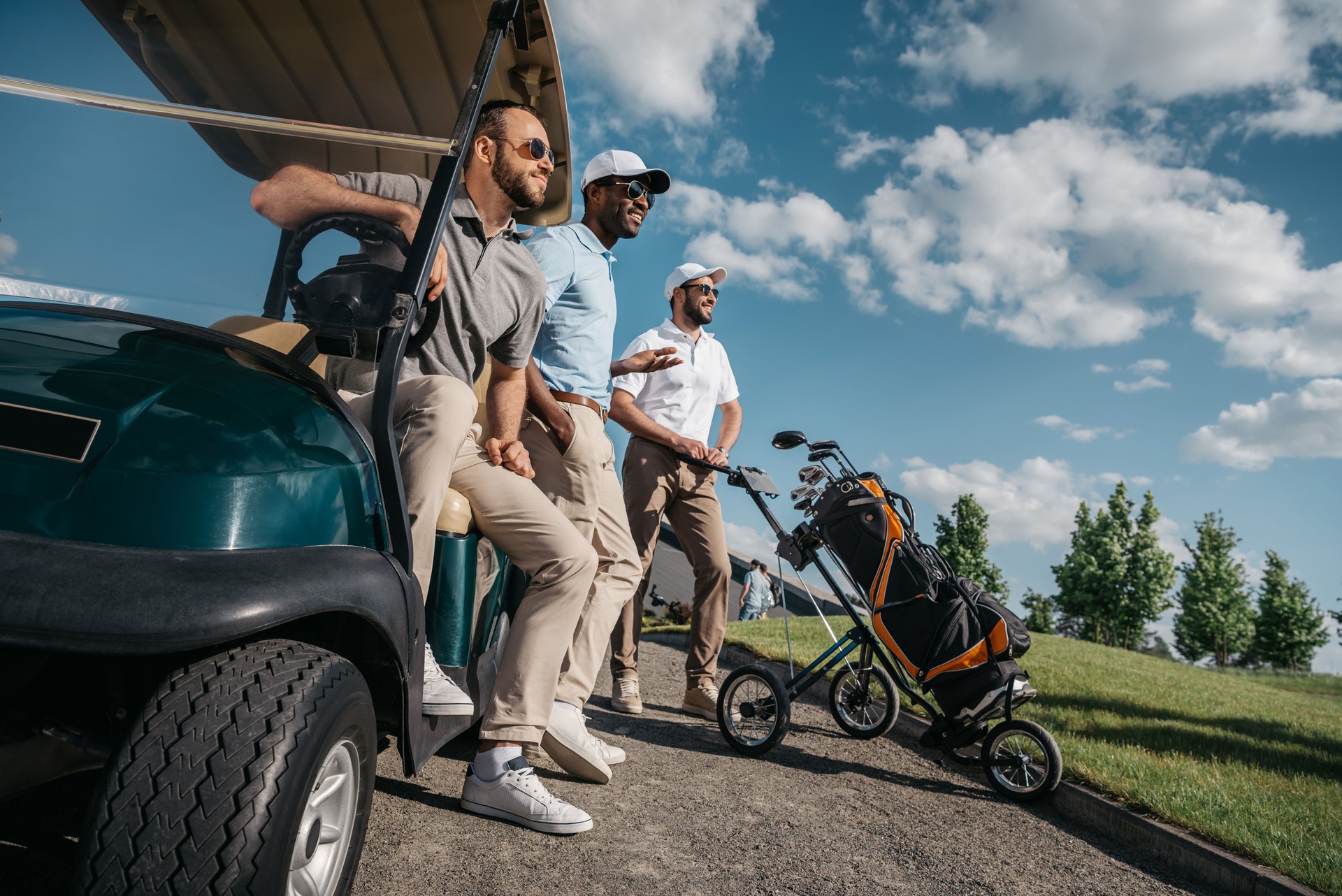 group of smiling friends standing near golf cart and looking away